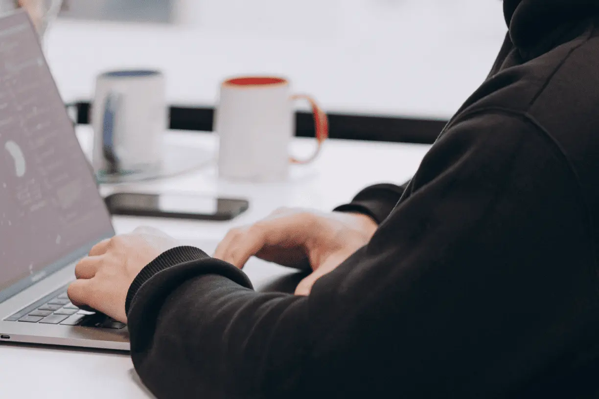 two hands over laptop during typing and two cups on table